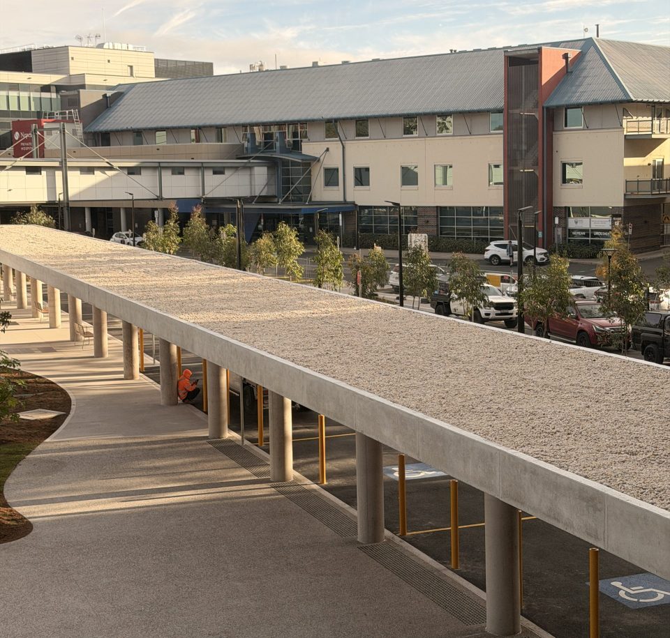 Elevated view along a covered walkway canopy at Nepean Hospital, Penrith NSW, with stabilised stone ballast across the roof and hospital buildings behind