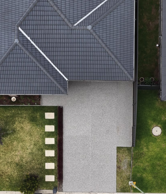 Aerial view of a light grey StoneSet resin-bound driveway running beside a home with a dark tiled roof and lawn with stepping pavers